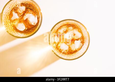 Zuschnitt von oben auf Gläser mit eisgekühltem Apfelsaft und goldenen Getränkeschatten auf hellem weißem Hintergrund Stockfoto