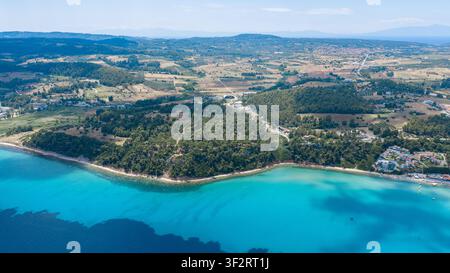 Luftbild über Kallithea, Griechenland, das eine bewaldete Landzunge zeigt, die sich in türkisblauem Wasser windet, mit einer sandigen Bucht und kleinen Resort-Gebäuden. Stockfoto