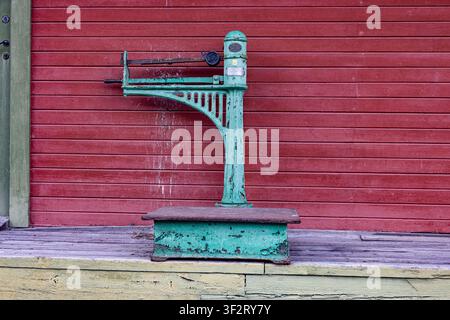 Mel-Stasjon, Rjukanbanen, Norwegen. Eine antike Waage steht vor einer roten Holzwand. Patinierte grüne Farbe zeigt Anzeichen von Witterungseinflüssen. Ihr stabiler Metallrahmen Stockfoto