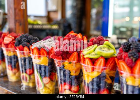 Verschiedene frisch geschnittene Fruchtstücke in klaren Plastikbechern, die auf Ladenregalen angeordnet sind. Gesunde Obstsalatbecher sind zum Verkauf bereit. Lebensmittel Stockfoto