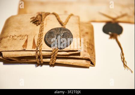 Alte Dokumente, die aus gealtertem Pergament oder Papier gefertigt sind. Sorgfältig gefaltet und sicher mit einem rustikalen Seil gebunden und mit einem kunstvollen Metallsiegel verziert. Stockfoto