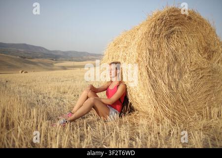 Junge Frau lehnt sich gegen einen Heuballen auf einem Feld Stockfoto