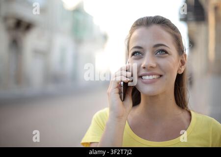 Fröhliche junge Frau lächelt, während sie draußen telefoniert Stockfoto