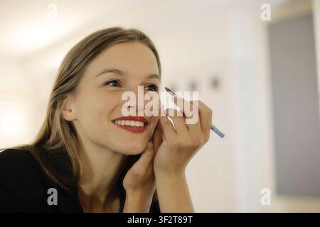 Junge Frau lächelt, während sie ihr Make-up macht Stockfoto