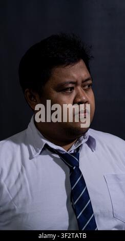 Ernsthafter erwachsener südostasiatischer Mann blickt scharf nach rechts vor einem pechschwarzen Hintergrund. Der übergewichtige Geschäftsmann trägt ein klassisches Stockfoto
