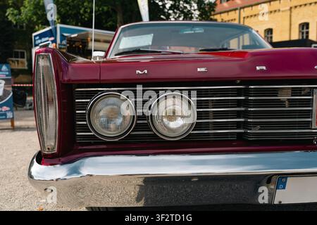 Berlin, Deutschland – 3. Mai 2026. Nahaufnahme von gepaarten Scheinwerfern, Chromgrill und burgunderroter Karosserie eines Oldtimer-Mercury-Autos, das auf der Oldtime-Ausstellung gezeigt wird Stockfoto