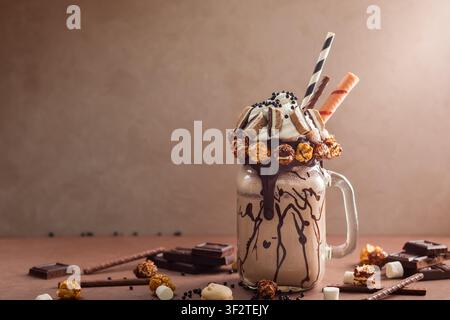 Schokoladenmilchshake mit Eis und Schlagsahne, Marshmallow, süßem Popcorn, Keksen, Waffeln, serviert in einem Glasmason-Glas. Stockfoto