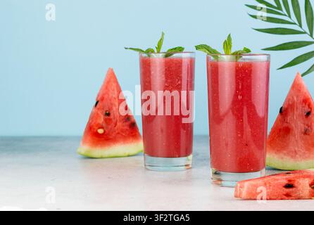 Frischer Wassermelonen-Smoothie in Gläsern, geschnittene Wassermelone auf blauem Hintergrund. Sommerliches Erfrischungsgetränk. Stockfoto