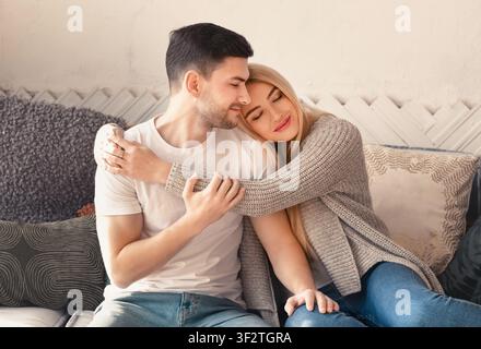 Glücklicher Mann und Frau, die sich auf dem Sofa im Wohnzimmer umarmt Stockfoto