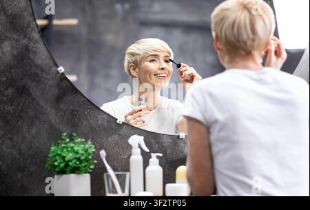 Frau, Die Make-Up Macht, Indem Sie Mascara Auf Wimpern Aufstellt, Die Im Badezimmer Stehen Stockfoto
