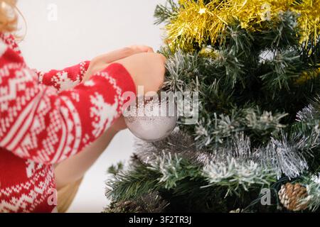 Kinderhände schmücken einen Weihnachtsbaum mit einem Ornament und feiern die Winterfeiertage Stockfoto