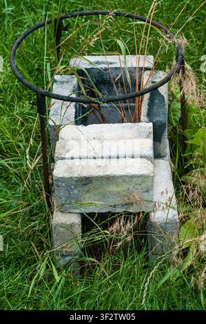 Ein verwittertes Betonblockgebäude mit einem verrosteten Metallringzaun ist von hohem grünem Gras und Wildpflanzen in einer Außenumgebung umgeben. Stockfoto
