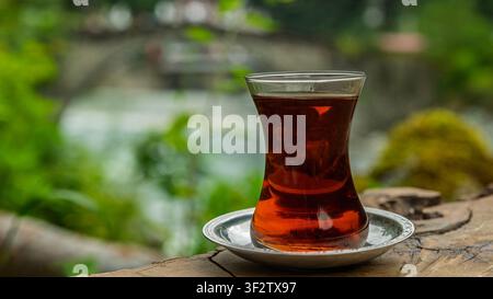 Traditioneller türkischer schwarzer Tee im Armudu-Glas mit Hintergrund des Firtina-Flusses Stockfoto