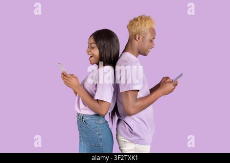 Seitenansicht eines jungen afroamerikanischen Paares mit Handys Violetter Studiohintergrund Stockfoto