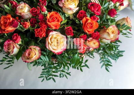 Die Hälfte eines Weidenkorbs, gefüllt mit frischen bunten Rosen, von oben fotografiert auf einem hellgrauen Hintergrund. Elegante Blumenarrangement mit großzügigem Stockfoto