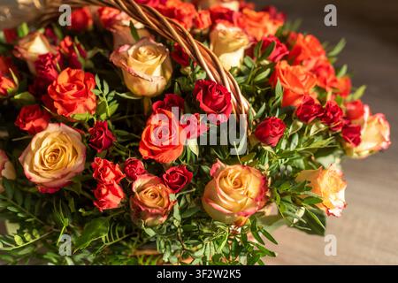 Die Hälfte eines Weidenkorbs, der mit frischen Rosen gefüllt ist, von der Seite fotografiert. Weiches Richtlicht betont die Blüten und den Korbboden vor einem Stockfoto