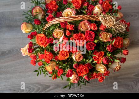 Oberansicht eines vollen Korbaus wicker, der mit bunten Rosen überquillt, auf einem dunkelgrauen Holzuntergrund. Elegante Blumenanordnung mit Kopierraum für gree Stockfoto