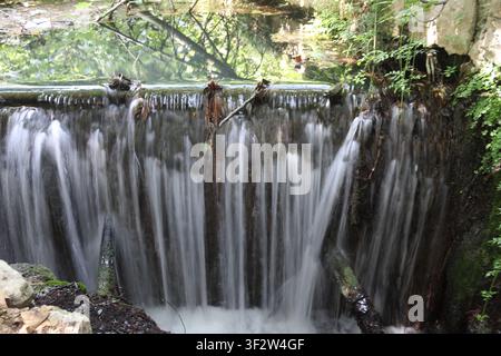 Nahaufnahme eines kleinen natürlichen Wasserfalls, der mit einem seidig glatten Bewegungseffekt in Albufera de Anna Naturpark in Valencia, Spanien, herabstürzt. Das klare Stockfoto