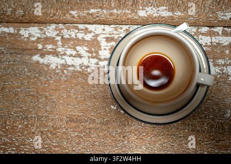 Top-Down-Ansicht einer fast leeren Keramikkoffeetasse mit einem restlichen braunen Tropfen auf einer Untertasse, die auf einem rustikalen verwitterten Holztisch ruht Stockfoto