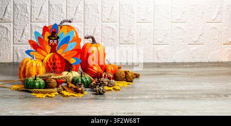 Festliche Thanksgiving-Ausstellung mit farbigem Truthahn, herbstlichen Kürbissen und natürlichem Dekor vor einer weißen Wand Stockfoto
