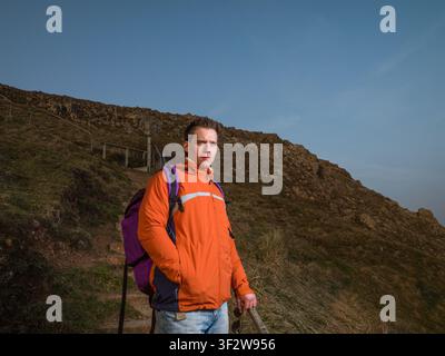 Porträt eines jungen Mannes in orangefarbener Jacke auf einem Hügel, der die Aussicht betrachtet Stockfoto