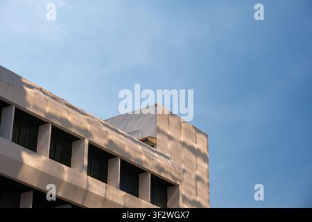 Minimalistische moderne Architektur mit einer weißen Gebäudefassade, die von Sonnenlicht beleuchtet und mit natürlichen Baumschatten unter einem klaren Blau dekoriert ist Stockfoto
