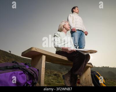 Junger Mann und ältere Frau, Wanderer, an einer Bank mit Karte, blicken über die Landschaft Stockfoto