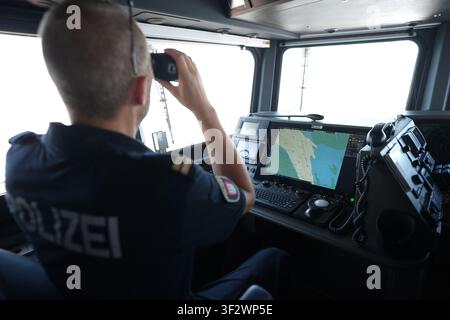 PRODUKTION - 13. Juli 2026, Niedersachsen, Cuxhaven: Alexander Wiegleb, Patrouillenleiter der Hamburger Wasserschutzpolizei, blickt durch ein Fernglas vom Steuerstand des seetüchtigen Küstenpatrouillenboots WS 1 ·Bürgermeister Brauer· auf der Brücke während einer Patrouille auf der Nordsee. Der Zuständigkeitsbereich des Wasserschutzpolizeireviers 4 (WSPK 4) erstreckt sich entlang der Elbe über 77 Seemeilen, von Tonne 105/106 vor Stade bis Tonne E 3, etwa 15 Seemeilen südlich von Helgoland, sowie das Hamburger Wattenmeer mit seinen Inseln Neuwerk, Scharhörn und Nigehörn. Foto: Marcus Brandt/dpa Stockfoto
