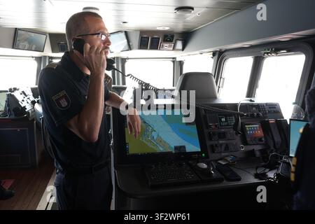PRODUKTION - 13. Juli 2026, Niedersachsen, Cuxhaven: Alexander Wiegleb, Patrouillenleiter der Hamburger Wasserpolizei, funkt ein Segelboot von der Brücke des seetüchtigen Küstenpatrouillenboots WS 1 ·Bürgermeister Brauer· während einer Patrouille auf der Nordsee. Der Zuständigkeitsbereich des Wasserpolizeireviers 4 (WSPK 4) erstreckt sich entlang der Elbe über 77 Seemeilen von Tonne 105/106 vor Stade bis Tonne E 3, etwa 15 Seemeilen südlich von Helgoland, sowie das Hamburger Wattenmeer mit seinen Inseln Neuwerk, Scharhörn und Nigehörn. Foto: Marcus Brandt/dpa Stockfoto
