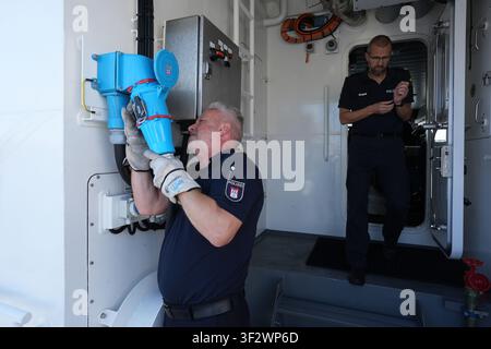 PRODUKTION - 13. Juli 2026, Niedersachsen, Cuxhaven: Stephan Amberge (links), Ingenieur der Hamburger Wasserschutzpolizei, trennt das Landstromkabel auf dem Deck des Offshore-Patrouillenboots WS 1 ·Bürgermeister Brauer· kurz vor einer Patrouille auf der Nordsee. Auf der rechten Seite des Fotos steht Alexander Wiegleb, Patrouillenkommandant der Hamburger Wasserschutzpolizei. Das Patrouillengebiet des Wasserschutzpolizeireviers 4 (WSPK 4) erstreckt sich entlang der Elbe über 77 Seemeilen von Tonne 105/106 vor Stade bis Tonne E 3, etwa 15 Seemeilen südlich von Helgoland, sowie das Hamburger Wattenmeer mit seinen Inseln Stockfoto