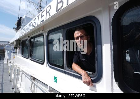 PRODUKTION - 13. Juli 2026, Niedersachsen, Cuxhaven: Alexander Wiegleb, Patrouillenleiter der Hamburger Wasserschutzpolizei, blickt aus einem Fenster auf der Brücke des seetüchtigen Küstenpatrouillenboots WS 1 ·Bürgermeister Brauer·, während es in die Elbe entlassen wird. Der Zuständigkeitsbereich des Wasserschutzpolizeireviers 4 (WSPK 4) erstreckt sich entlang der Elbe über 77 Seemeilen von Tonne 105/106 nahe Stade bis zur Tonne E 3, etwa 15 Seemeilen südlich von Helgoland, sowie das Hamburger Wattenmeer mit seinen Inseln Neuwerk, Scharhörn und Nigehörn. Foto: Marcus Brandt/dpa Stockfoto