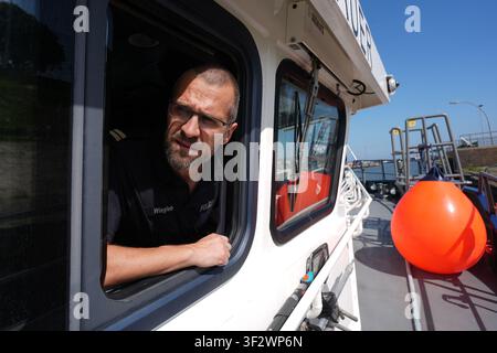 PRODUKTION - 13. Juli 2026, Niedersachsen, Cuxhaven: Alexander Wiegleb, Patrouillenleiter der Hamburger Wasserschutzpolizei, blickt aus einem Fenster auf der Brücke des seetüchtigen Küstenpatrouillenboots WS 1 ·Bürgermeister Brauer·, während es in die Elbe entlassen wird. Der Zuständigkeitsbereich des Wasserschutzpolizeireviers 4 (WSPK 4) erstreckt sich entlang der Elbe über 77 Seemeilen von Tonne 105/106 nahe Stade bis zur Tonne E 3, etwa 15 Seemeilen südlich von Helgoland, sowie das Hamburger Wattenmeer mit seinen Inseln Neuwerk, Scharhörn und Nigehörn. Foto: Marcus Brandt/dpa Stockfoto