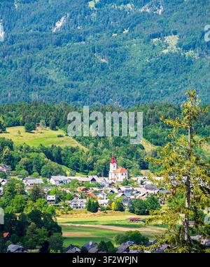 Panoramablick auf die Landschaft unter den Julischen Alpen in Slowenien, mit einem malerischen Dorf mit einer Kirche im Zentrum, umgeben von Grün Stockfoto