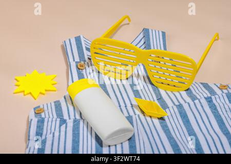 Konzept eines sicheren Strandurlaubs und sorgfältiger Kinderbetreuung während eines Urlaubs. Baby-Sommerutensilien Flat Lay, gestreifter Strampler, Strohhut und Sonnenschutzlos Stockfoto