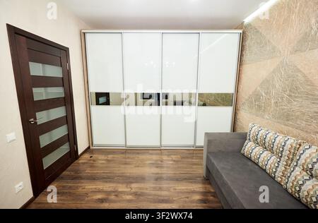 Polstersofa in einem zeitgenössischen Raum mit Schiebeschrank, gemusterter Wandverkleidung und dunklem Holzboden platziert. Wohnraumgestaltung, Lebensstil und Renovierungskonzept Stockfoto