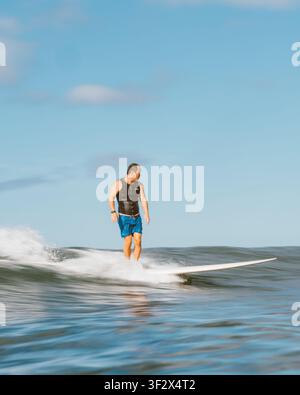 ALA MOANA BOWLS, HONOLULU, HAWAII - 1. APRIL 2022: Ein Mann in einer Schwimmweste und blauen Shorts tritt auf seinem Longboard zurück. Stockfoto