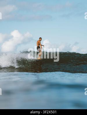 ALA MOANA BOWLS, HONOLULU, HAWAII - 1. APRIL 2022: Ein Mann schiebt sein Longboard entlang einer sauberen Welle in Boardshorts. Stockfoto