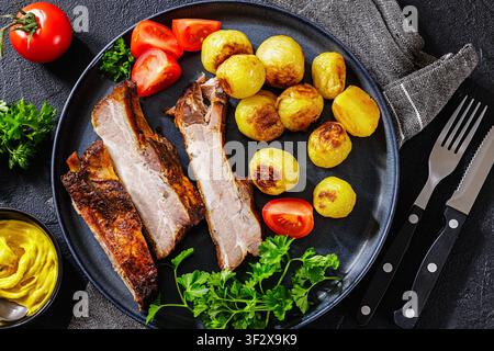 Amerikanische gegrillte Schweinerippchen aus dem Hinterhof mit zarten, gewürzten ganzen Kartoffeln, frischen Gartentomaten, lockiger Petersilie und klassischem amerikanischem gelbem Baseballschläger Stockfoto