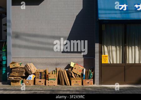 Stapel ordentlich gestapelter Pappkartons säumen den Bürgersteig, was das tägliche Leben und die Recyclinggewohnheiten in der Stadt widerspiegelt. Die unscheinbare Fassade hin Stockfoto