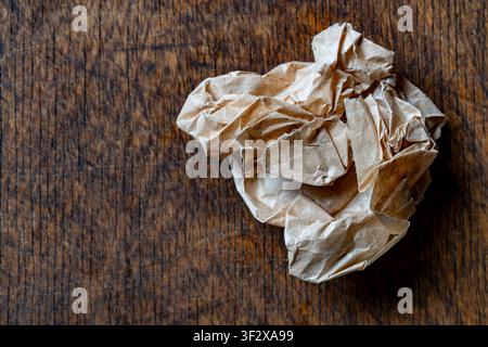 Zerknüllter brauner Papierball auf dunklem Holztisch mit Kopierraum, Nahaufnahme. Strukturierter Recycling-Papiermüll, der einen Fehler oder den Brainstorming-Prozess symbolisiert. Stockfoto