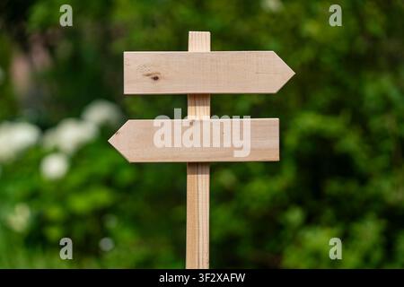 Leerer hölzerner Schildpfosten mit zwei Pfeilen, die in entgegengesetzte Richtungen zeigen, auf einem verschwommenen grünen Gartenhintergrund für Kopierraum für Geschäftsentscheidungen Navigati Stockfoto