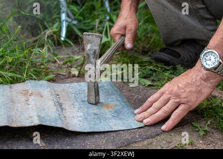 Arbeiter hält Stahlplatte und hämmert Nahaufnahme Stockfoto
