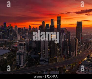 Luftbild der Skyline von Melbourne bei Sonnenaufgang, mit modernen Wolkenkratzern in Southbank, beleuchtet von einem lebendigen orangefarbenen Himmel über der Stadtautobahn Stockfoto