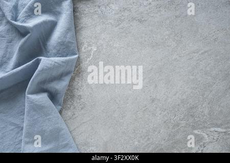 Weicher blauer Leinenstoff auf grauem Steinhintergrund mit Kopierraum. Minimaler Textilhintergrund für Küchen- und Wohnstyling. Stockfoto