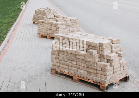 Betonplatten, die auf Holzpaletten gestapelt sind, bereit für den Bau eines neuen Gehwegs oder die Straßenwartung neben einer Straße Stockfoto