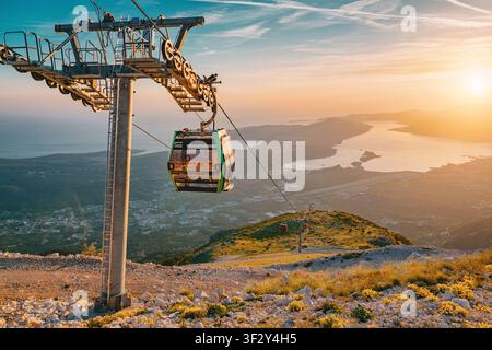 Seilbahn steigt einen schroffen Berghang hinauf, während ein dramatischer Sonnenuntergang die Bucht von Kotor und das Adriatische Meer unten beleuchtet Stockfoto