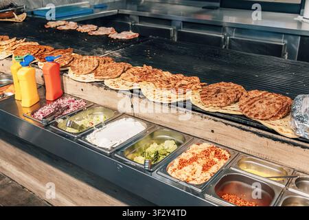Frische Kebabs und Fladenbrot auf einem Holzkohlegrill grillen, mit einer großen Auswahl an Soßen und frischen Zutaten Stockfoto