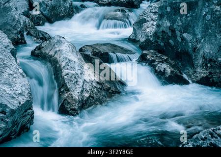 Flusswasser fließt schnell über große Natursteine und schafft kleine Wasserfälle und eine dynamische, frische Bergbachszene Stockfoto