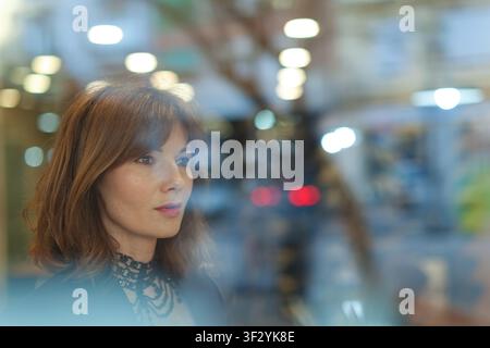 Frau schaut durch ein Glasfenster in einer städtischen Umgebung Stockfoto