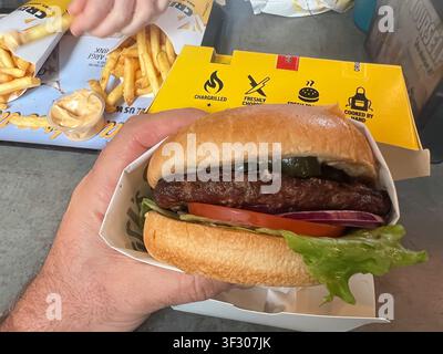 SYDNEY - JULI 08 2026: Eine Ego-Perspektive-Aufnahme eines Mannes, der einen saftigen Gourmet-Rindfleischburger mit Jalapeños, Guacamole und triefendem Ch Stockfoto